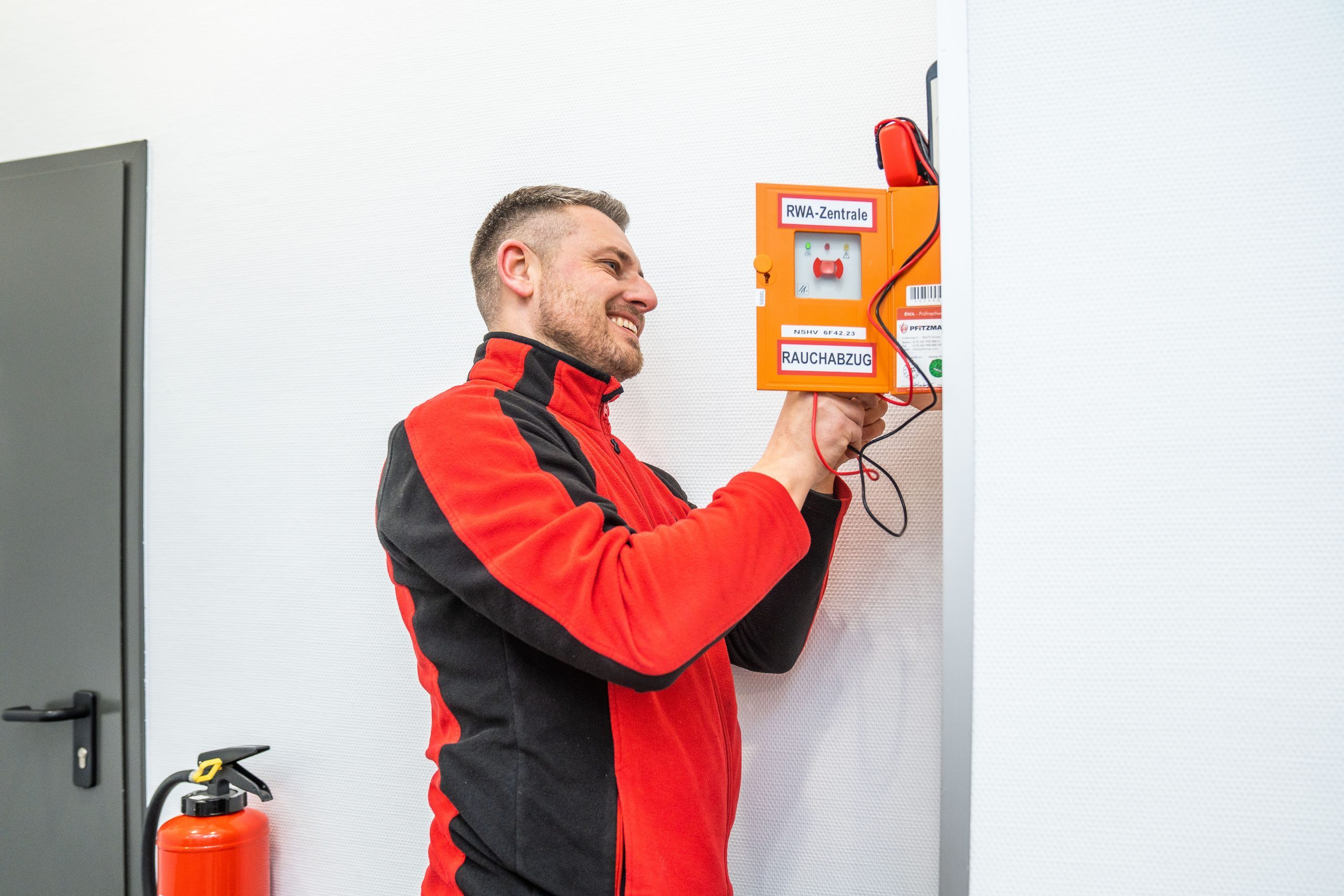 Servicetechniker von Pfitzmayr Brandschutztechnik prüft die orangefarbene RWA-Zentrale für den Rauchabzug.